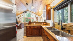 Een keuken met houten kastjes, granieten aanrecht, een roestvrijstalen spoelbak en een groot raam met uitzicht op een bos.