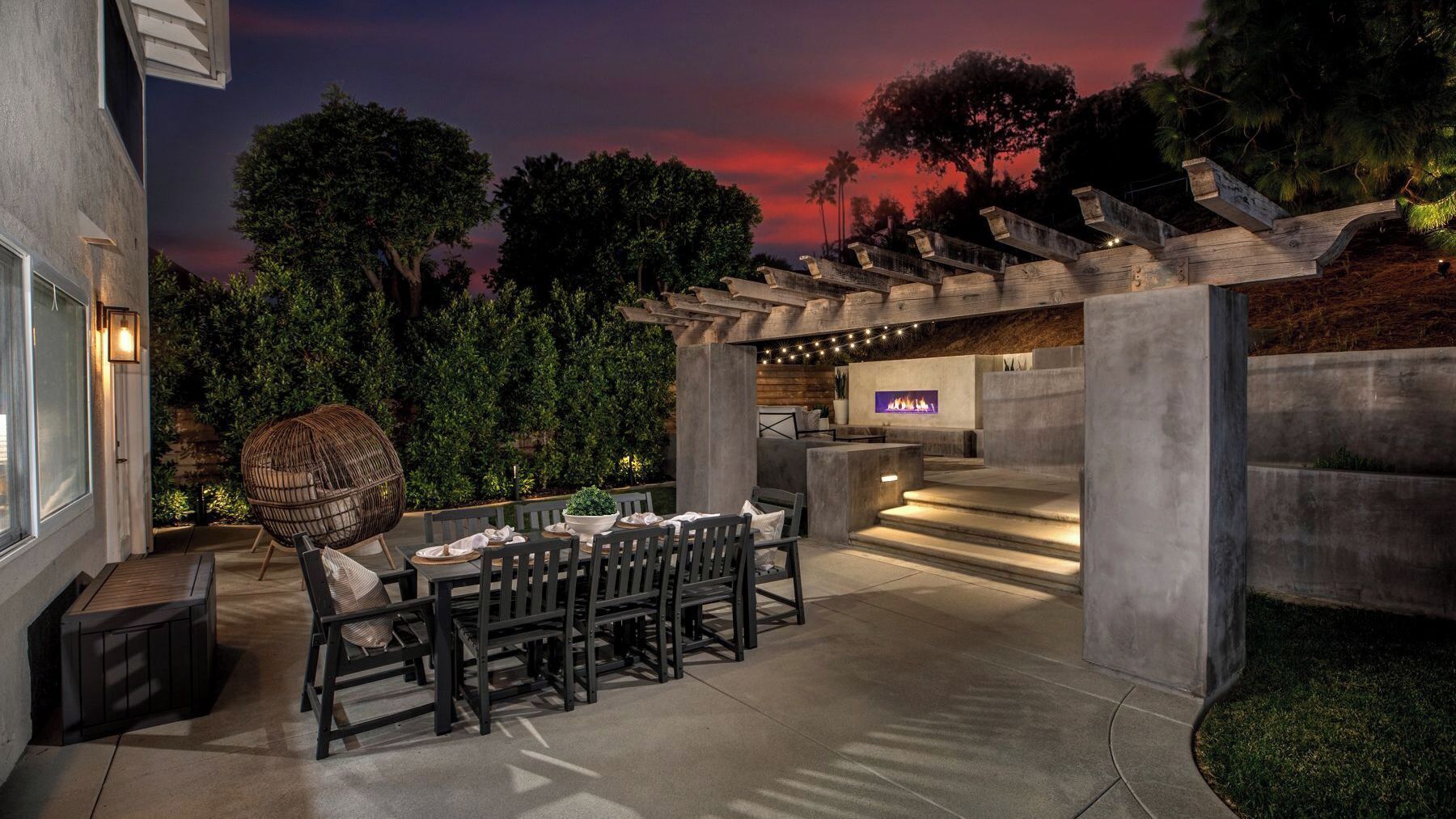 Un patio al aire libre con una mesa de comedor y sillas, un muro de piedra y una pérgola.