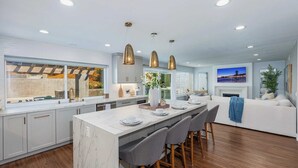 Une cuisine moderne dotée d’un îlot en marbre, de luminaires suspendus et d’une grande fenêtre donnant sur un jardin.