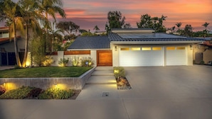 Une maison moderne à deux étages, dotée d’un garage, d’une pelouse bien entretenue et offrant une vue sur un ciel au coucher du soleil.