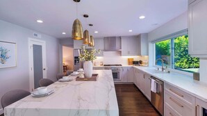 Une cuisine moderne avec un îlot en marbre, des luminaires suspendus et une vue sur la verdure environnante.