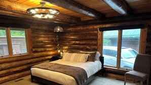 A log cabin bedroom with a bed, a chair, and a large window. - Ocean Front Property with Beach Access (Ketchikan)