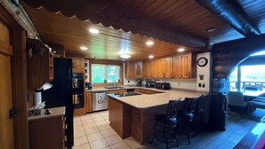A spacious kitchen with wooden cabinets, a large island with bar stools, a built-in oven, and a dishwasher. - Ocean Front Property with Beach Access (Ketchikan)