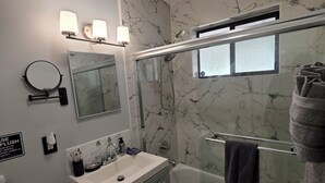 Un baño moderno con salpicadero de mármol, ducha con mampara de vidrio, tocador con lavabo y un inodoro.