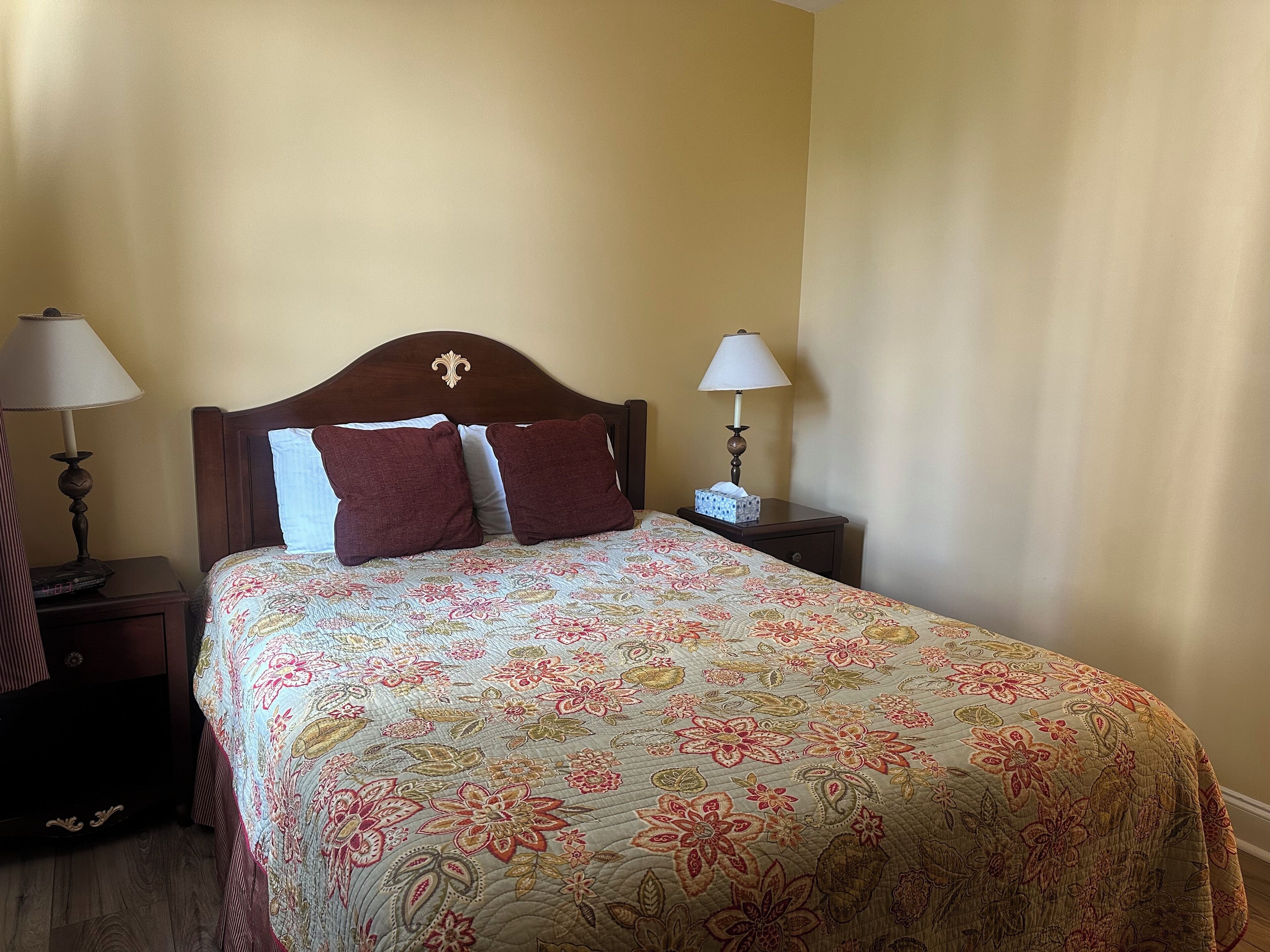 Una cama bien hecha con una colcha floral, dos lámparas de noche y una mesita de noche con una caja de pañuelos.
