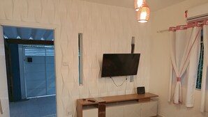 Une chambre d’hôtel dotée d’un téléviseur à écran plat fixé au mur, d’une console en bois, d’un petit tapis et d’un lit recouvert d’une couvre-lit à motifs floraux.