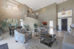 A spacious living room with a high ceiling, a staircase, and a dining area.