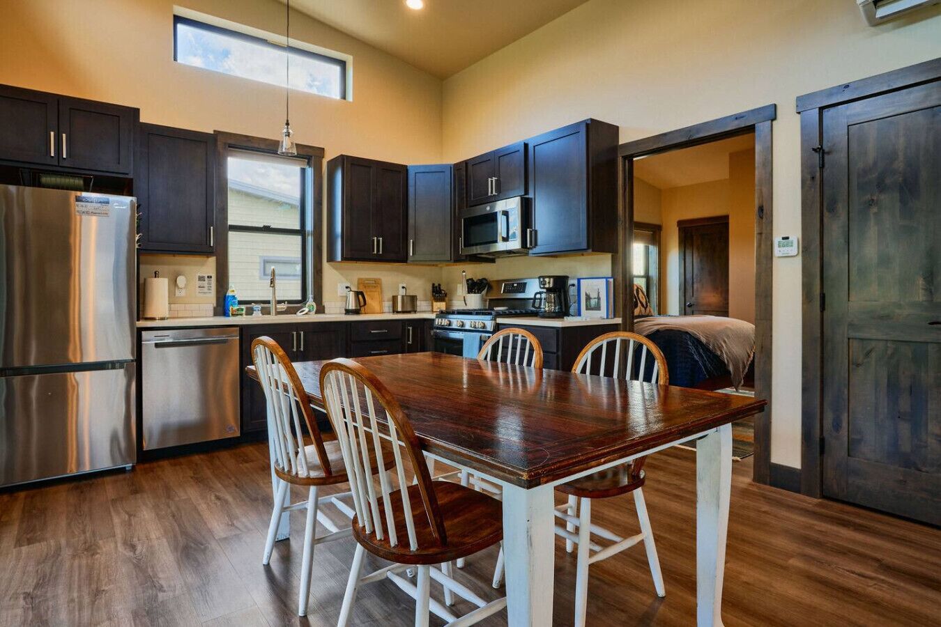 A modern kitchen with dark cabinets, stainless steel appliances, and a wooden dining table with chairs.
