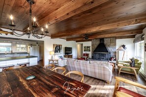 Un amplio salón con techo de madera, chimenea y una mesa de comedor con sillas.