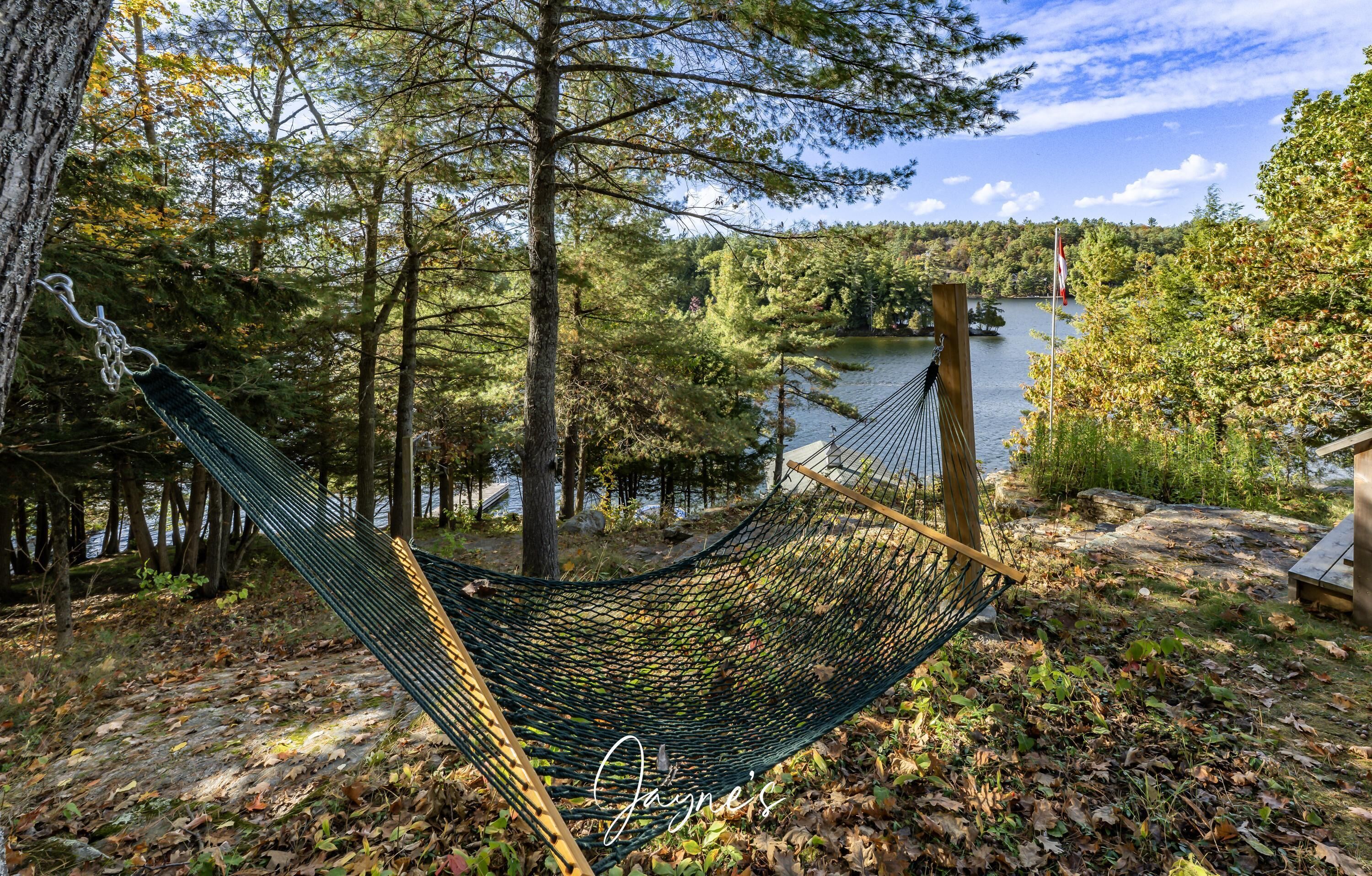 A hammock in a wooded area with a lake and a flag in the background.