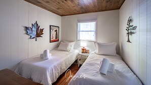 Una habitación con dos camas individuales, una mesita con lámpara, una ventana y adornos en la pared, incluyendo una hoja de arce y un cuadro enmarco.