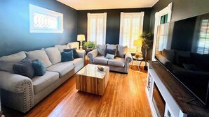 Ein Wohnzimmer mit einem beigen Sofa, einem Holztisch und einem Fernseher auf einem Schrank.