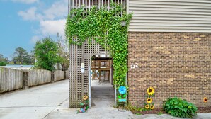 A wooden gate with a climbing vine, a brick wall, and a concrete pathway leading to a building entrance. - Sunflower Theater - 3br, 2ba, 5 beds, 1600sqft with Smart Projector Movie Screen (Wilmington)