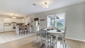 A spacious kitchen with white cabinetry, a dining area with a white table and chairs, and a large window with blinds. - Sunflower Theater - 3br, 2ba, 5 beds, 1600sqft with Smart Projector Movie Screen (Wilmington)