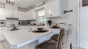 A modern kitchen with white cabinetry, a large island, and a woven chair. - Sunflower Theater - 3br, 2ba, 5 beds, 1600sqft with Smart Projector Movie Screen (Wilmington)
