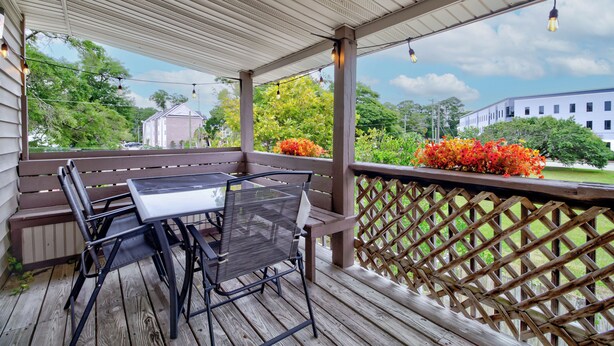 A covered outdoor area with a wooden deck, a table with chairs, and a view of buildings and trees in the background. - Sunflower Theater - 3br, 2ba, 5 beds, 1600sqft with Smart Projector Movie Screen (Wilmington)