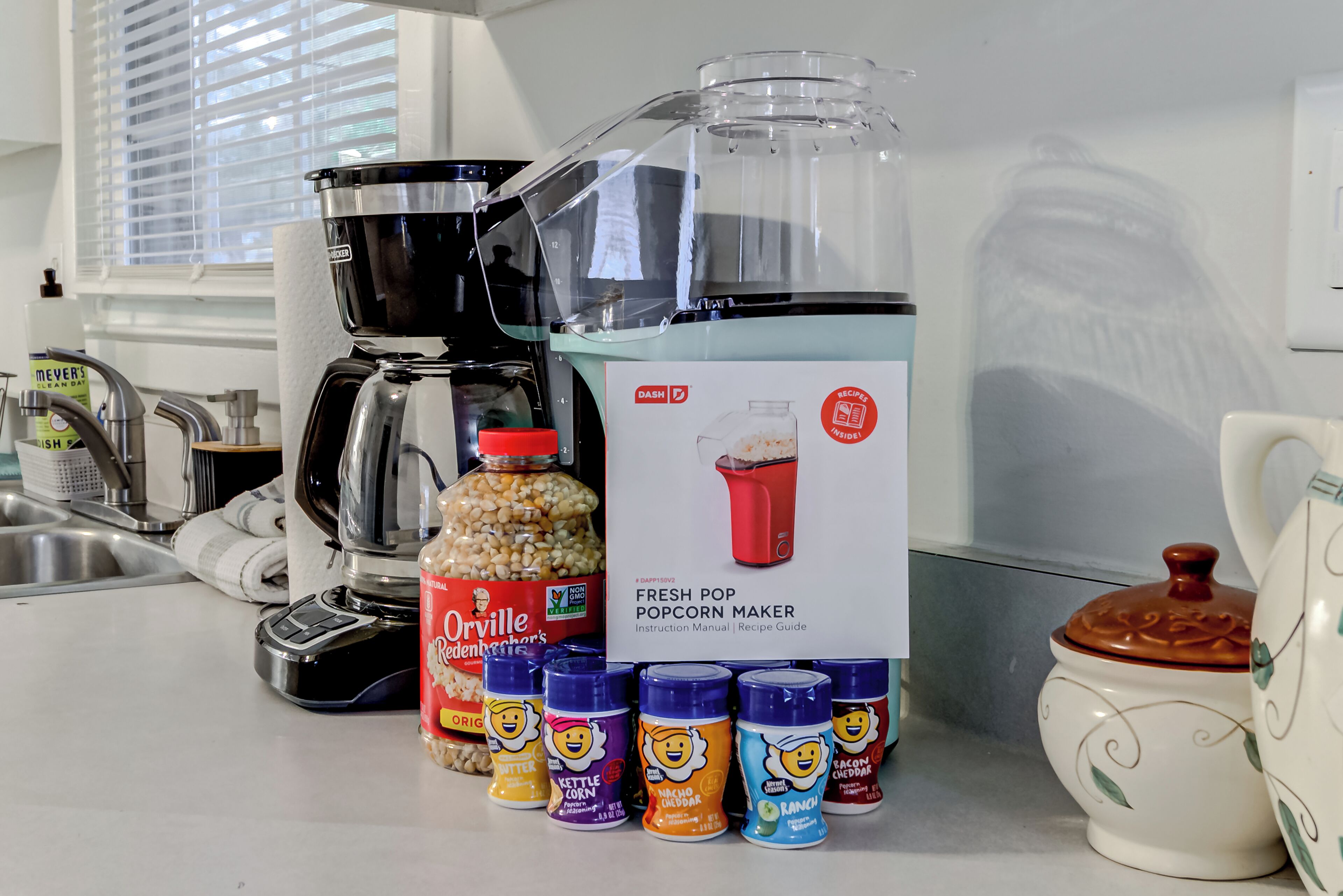 Een keukenblad met een nieuwe popcornmachine, een koffiezetapparaat en verschillende kruidenflesjes.