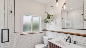 A modern bathroom with white subway tiles, a white toilet, a vanity with a wooden countertop, and a large mirror. - Amazing cottage in sunny Tampa close to everything. (Tampa)
