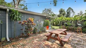 A patio with a wooden table and benches, surrounded by a brick floor and a variety of plants. - Amazing cottage in sunny Tampa close to everything. (Tampa)