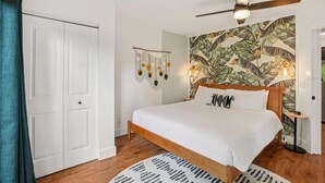 A bedroom with a bed, a ceiling fan, a wall with a tropical leaf pattern, and a door. - Amazing cottage in sunny Tampa close to everything. (Tampa)