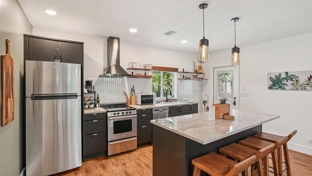 A modern kitchen with stainless steel appliances, a central island with bar stools, and pendant lighting. - Amazing cottage in sunny Tampa close to everything. (Tampa)