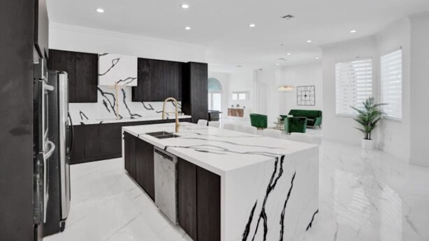 A modern kitchen with a marble island, dark cabinetry, and a large window providing natural light. - 7000sf Mansion w/ Pool/Gameroom/Theater - N (Davie)
