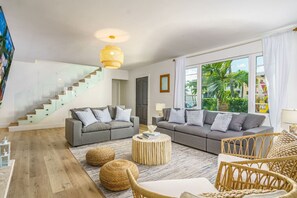 Un salon moderne avec un canapé gris, un fauteuil en osier, une table basse ronde et un escalier doté de rampes en verre.