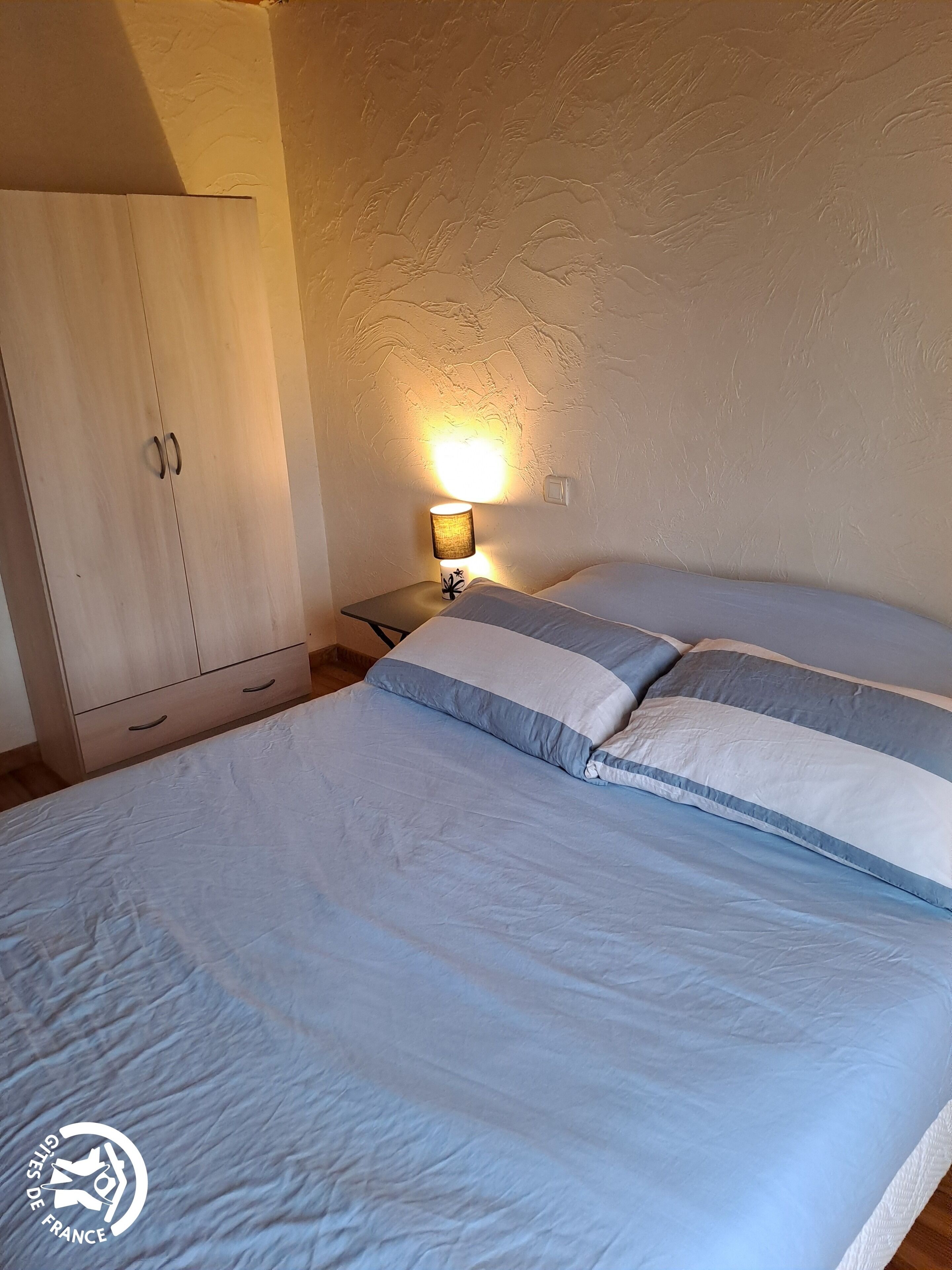 A bedroom with a bed, a nightstand, a lamp, and a wardrobe.