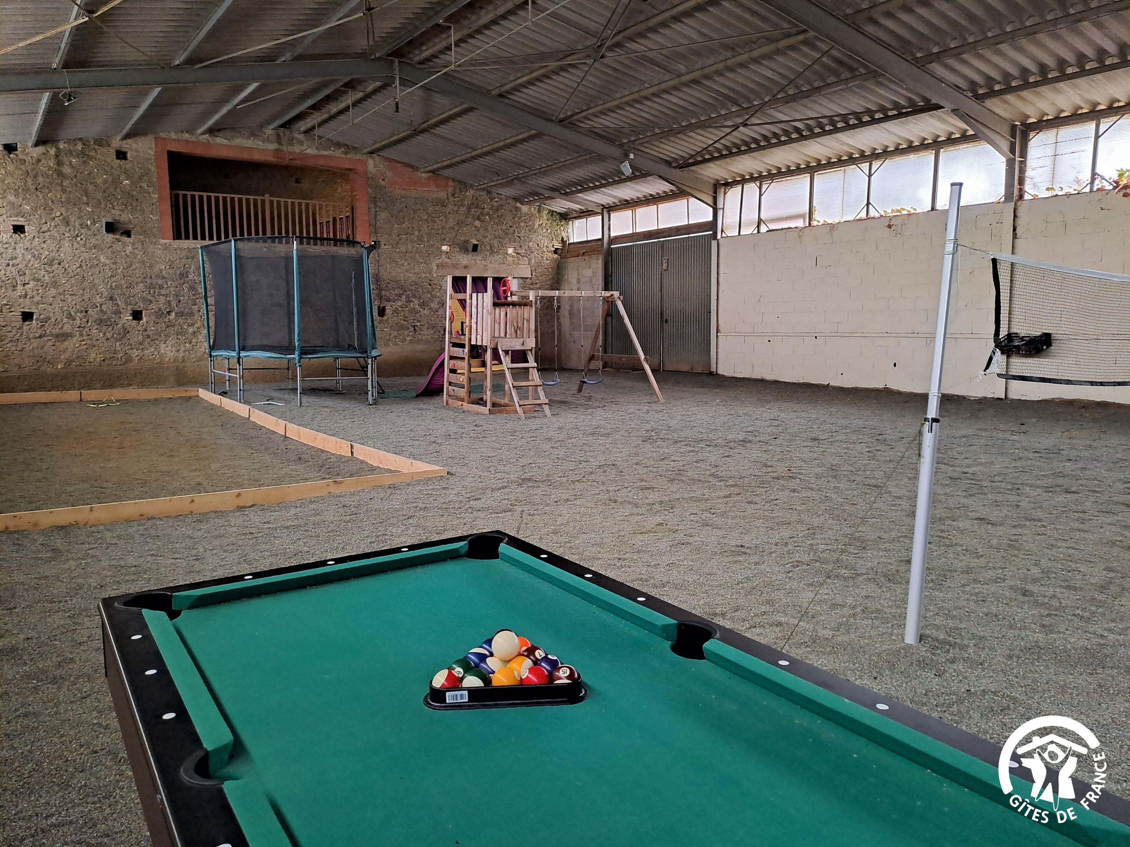 Ein Billardtisch mit Kugeln, ein Trampolin und eine Kletterstruktur in einem überdachten Innenbereich.