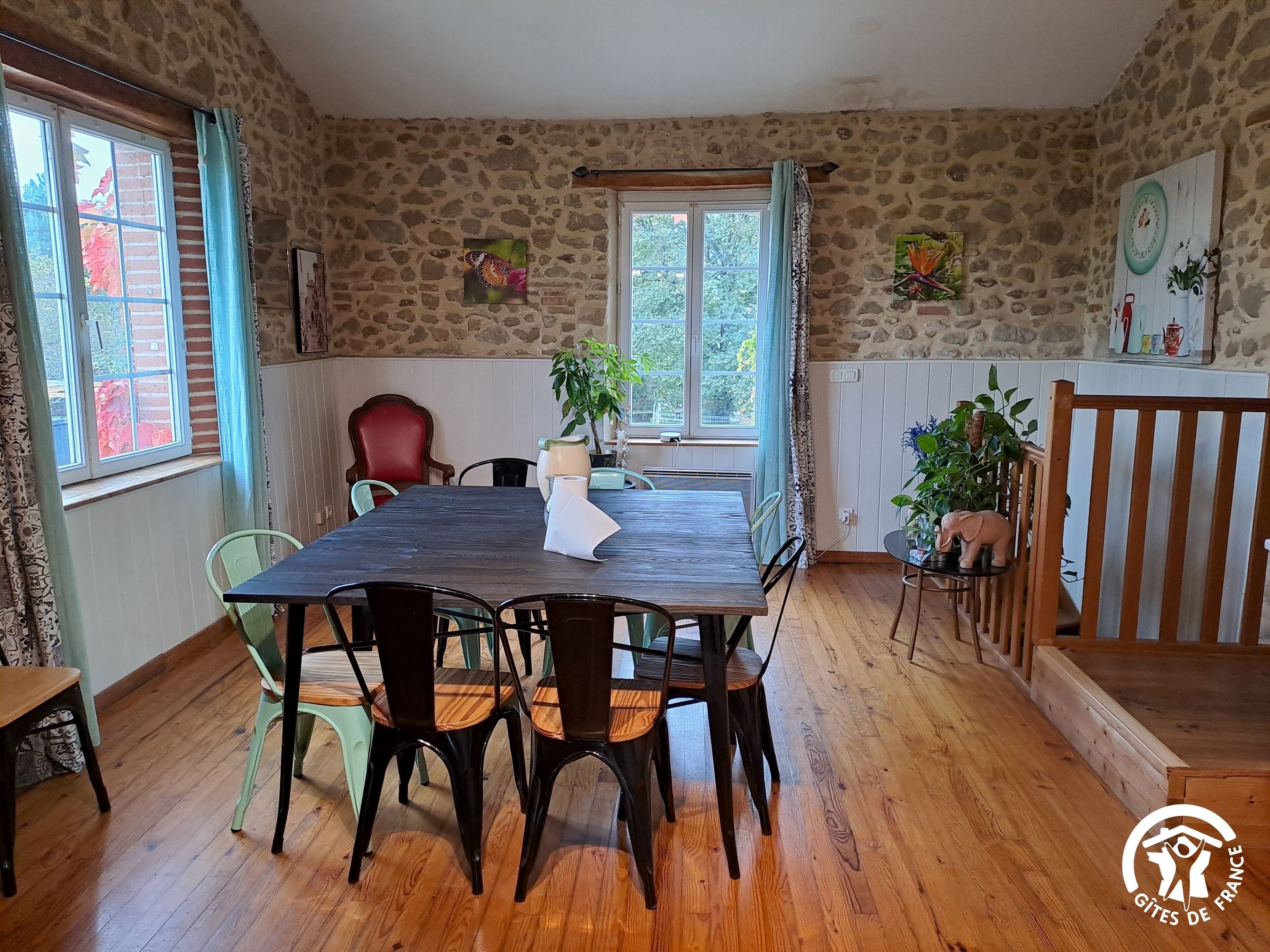 A dining area with a wooden table and chairs, stone walls, and a view of greenery outside.