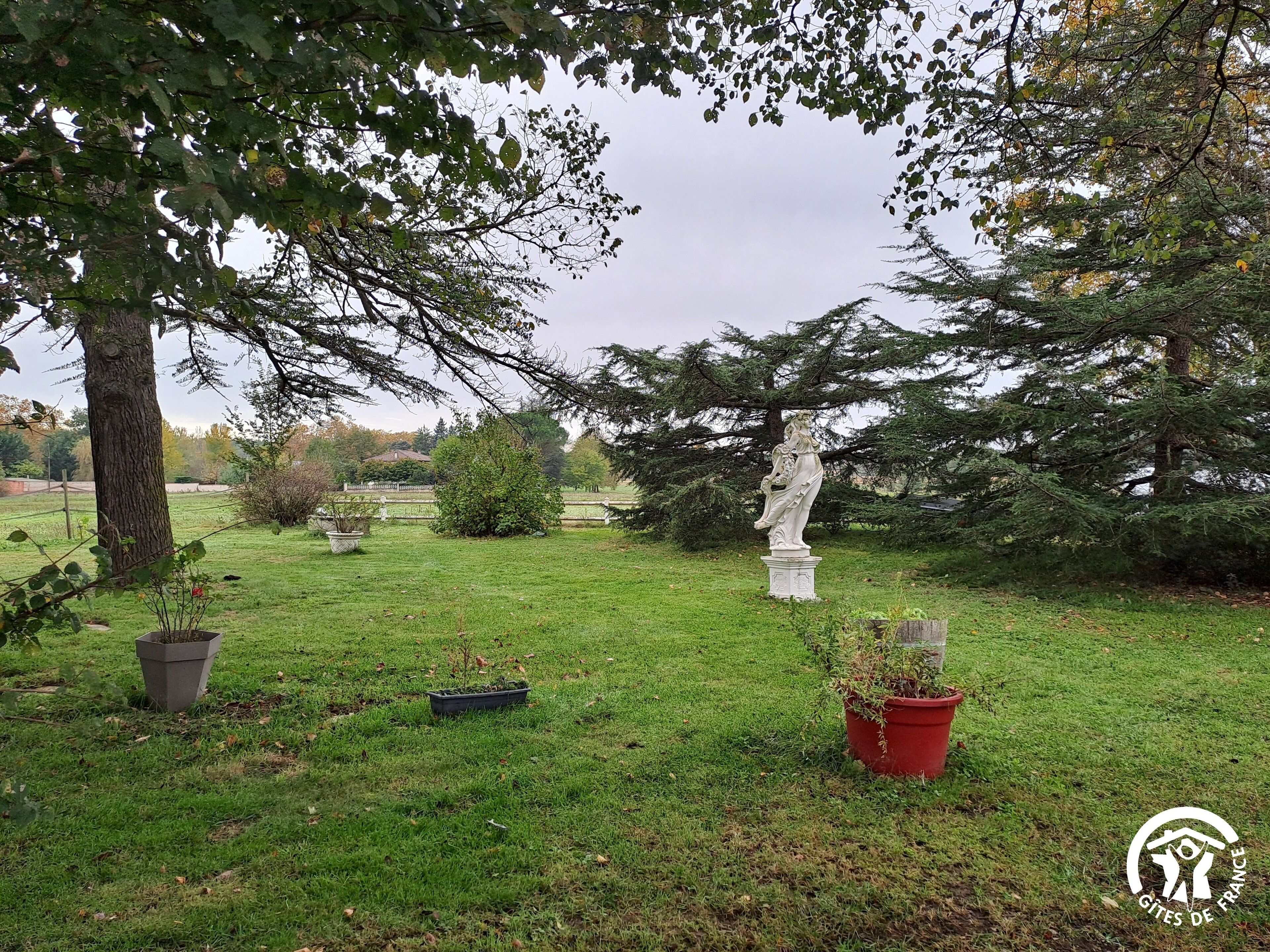 A park with a statue, trees, and potted plants.