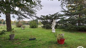 A park with a statue, trees, and potted plants.