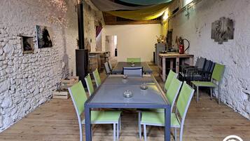 A rustic dining area with a stone wall, wooden floor, and a long table with chairs.