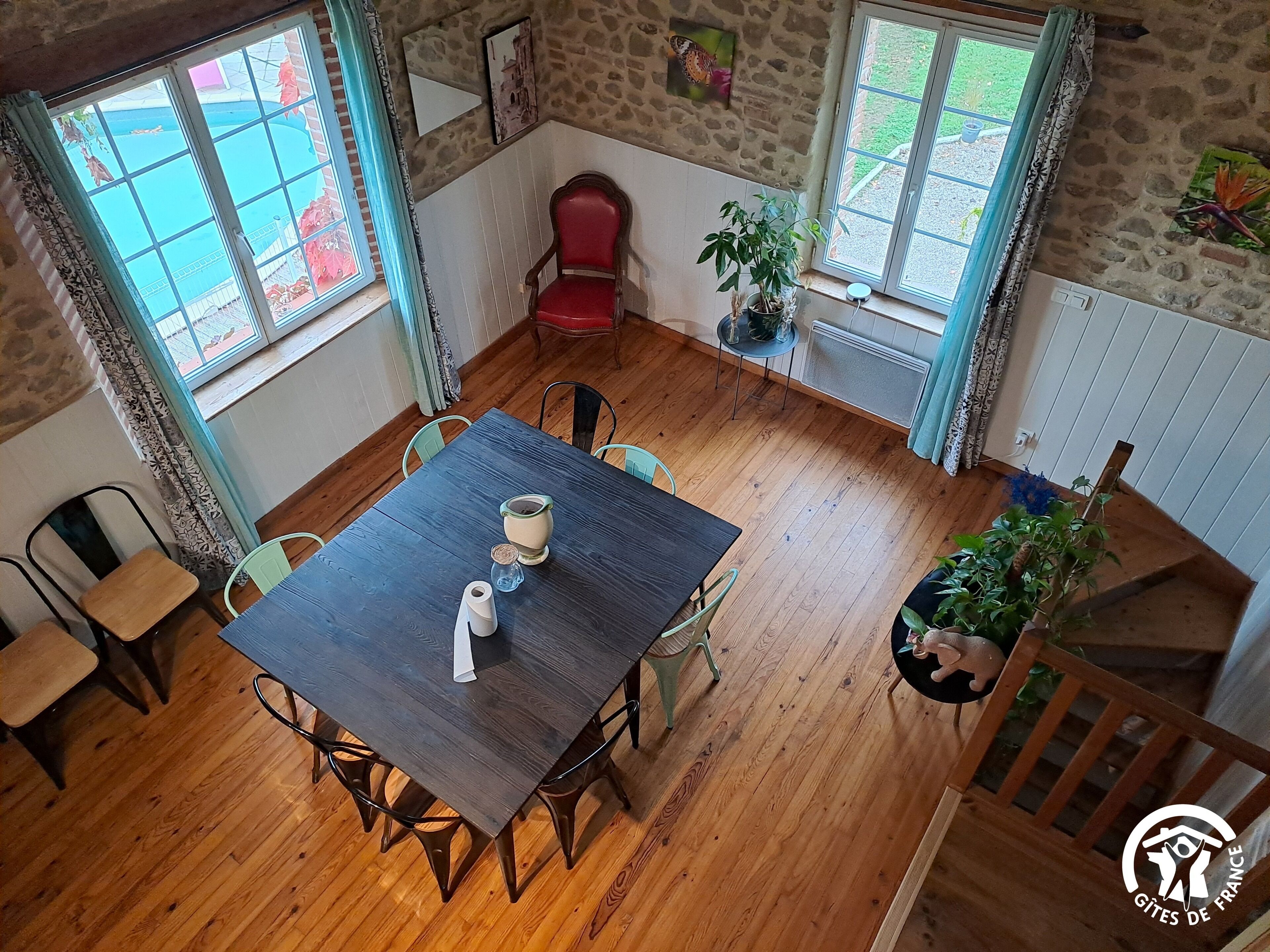 Un comedor con una mesa de madera, sillas, una silla roja, plantas en macetas y vistas por una ventana.