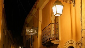 Ein Steinhaus mit einem 'HOTEL'-Schild, einem Balkon mit schmiedeeisernem Geländer und Blumentöpfen im Erdgeschoss.