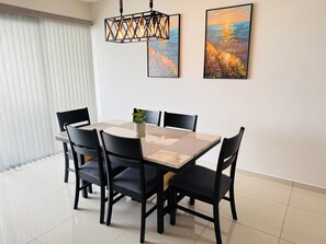 A dining area with a round table, six chairs, a potted plant, and two paintings on the wall.