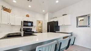 Una cocina moderna con armarios blancos, una isla central con taburetes y un refrigerador negro y un microondas.