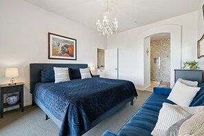 A bedroom with a large bed, a blue sofa, a chandelier, and a painting on the wall. - Luxury Condo (Scottsdale)