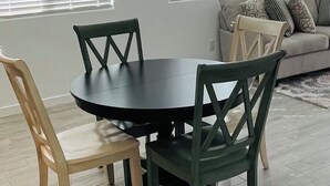 En spiseplads med et rundt bord, fire stole, en sofa og et vindue med persienner.