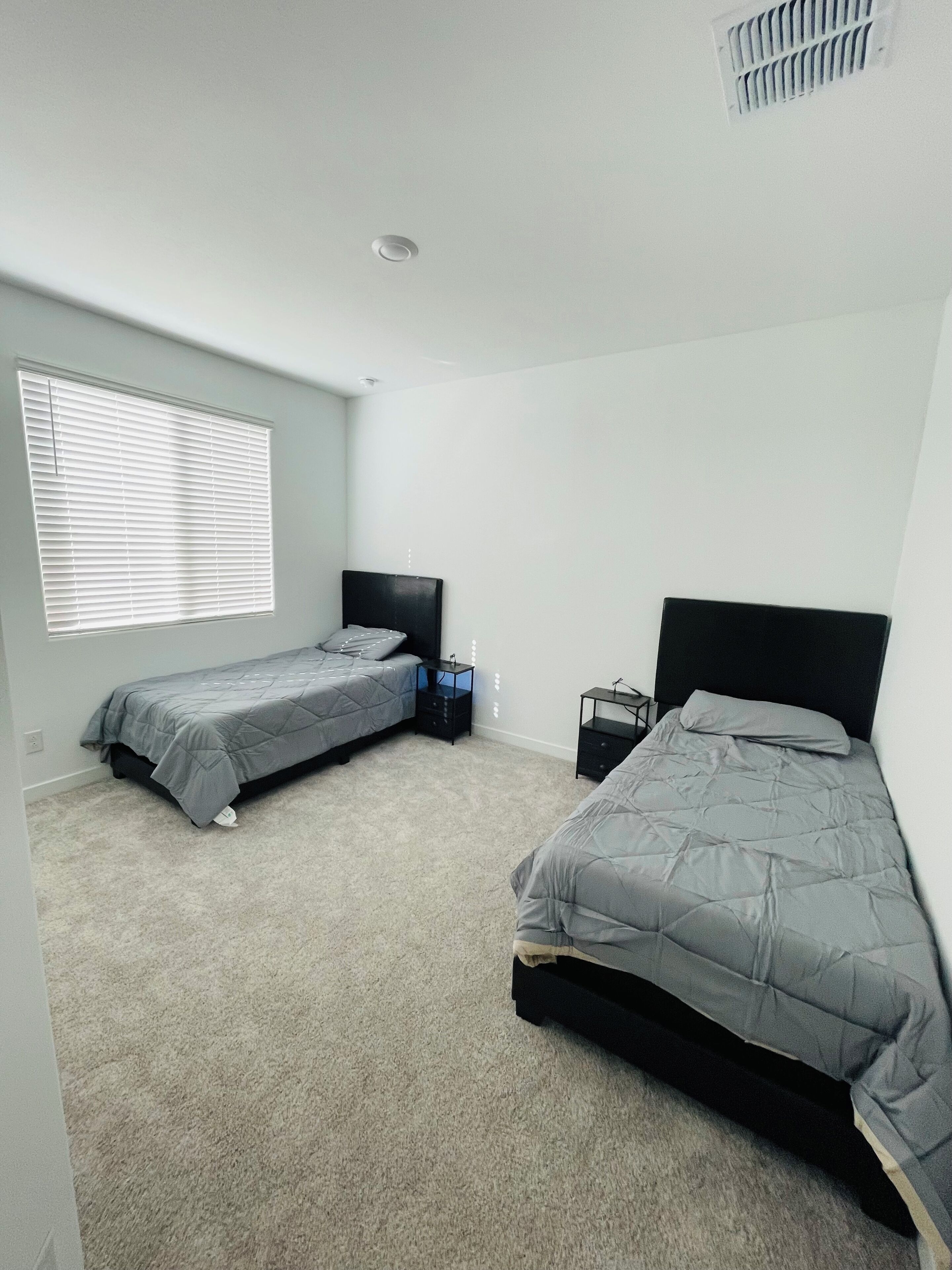 Ein Schlafzimmer mit zwei Einzelbetten, einem Fenster mit Jalousien, einem Deckenventilator und einem Teppichboden.