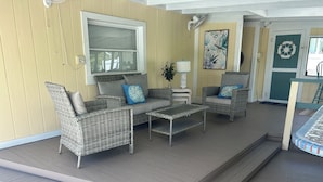 A covered outdoor seating area with wicker furniture, a table, and a wall-mounted fan.