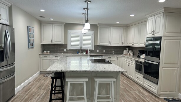 A modern kitchen with white cabinets, granite countertops, stainless steel appliances, and a central island with bar stools.