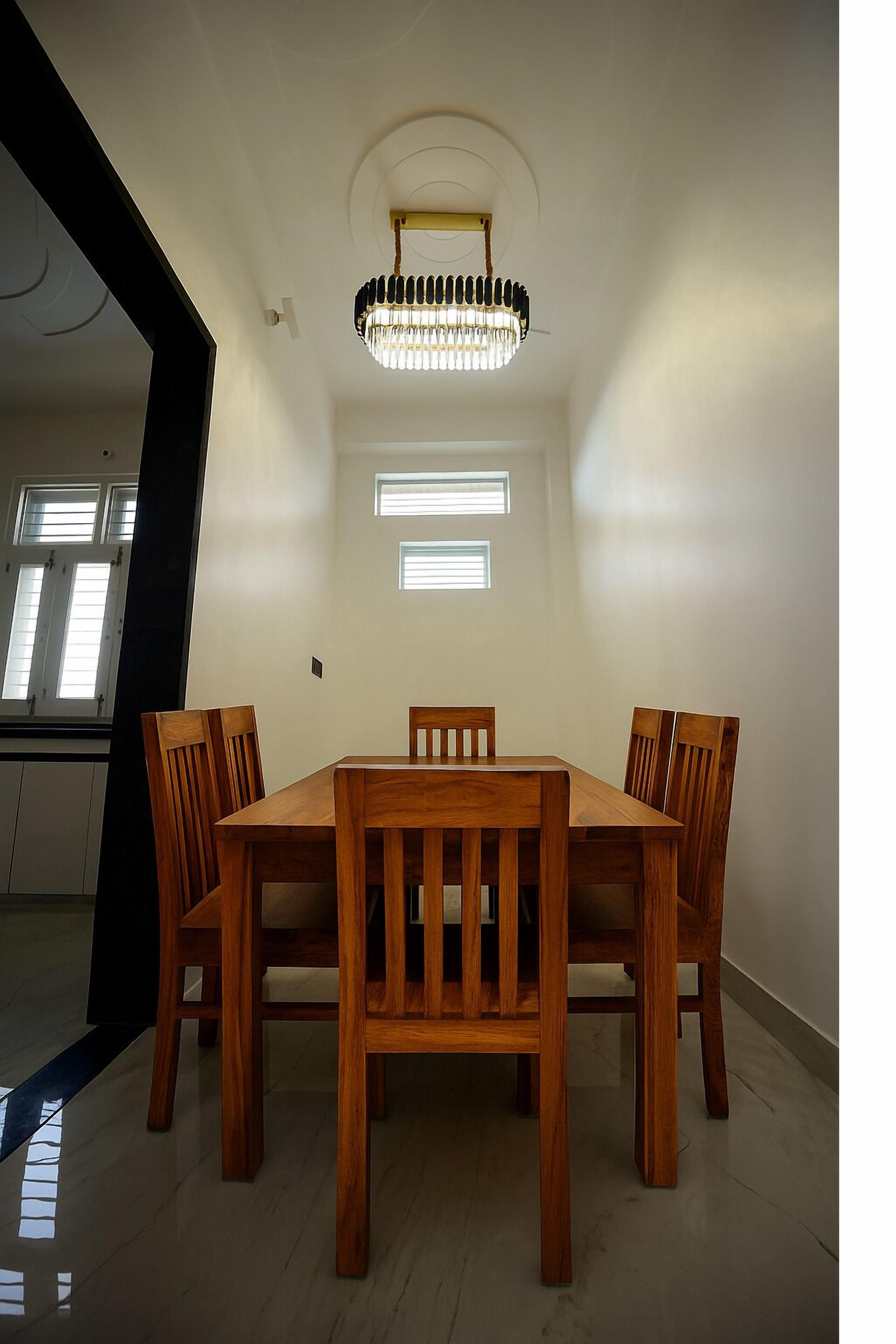 Un coin repas avec une table et des chaises en bois, un lustre et une fenêtre équipée de stores.