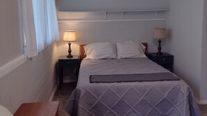 Un dormitorio con una cama, dos mesitas de noche con lámparas, un ventilador de techo y una ventana con cortinas.