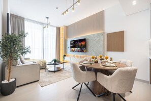 A modern living room with a sofa, dining table, chairs, and a TV mounted on the wall. - Binghatti Suites by Hostiva - City View (Dubai)
