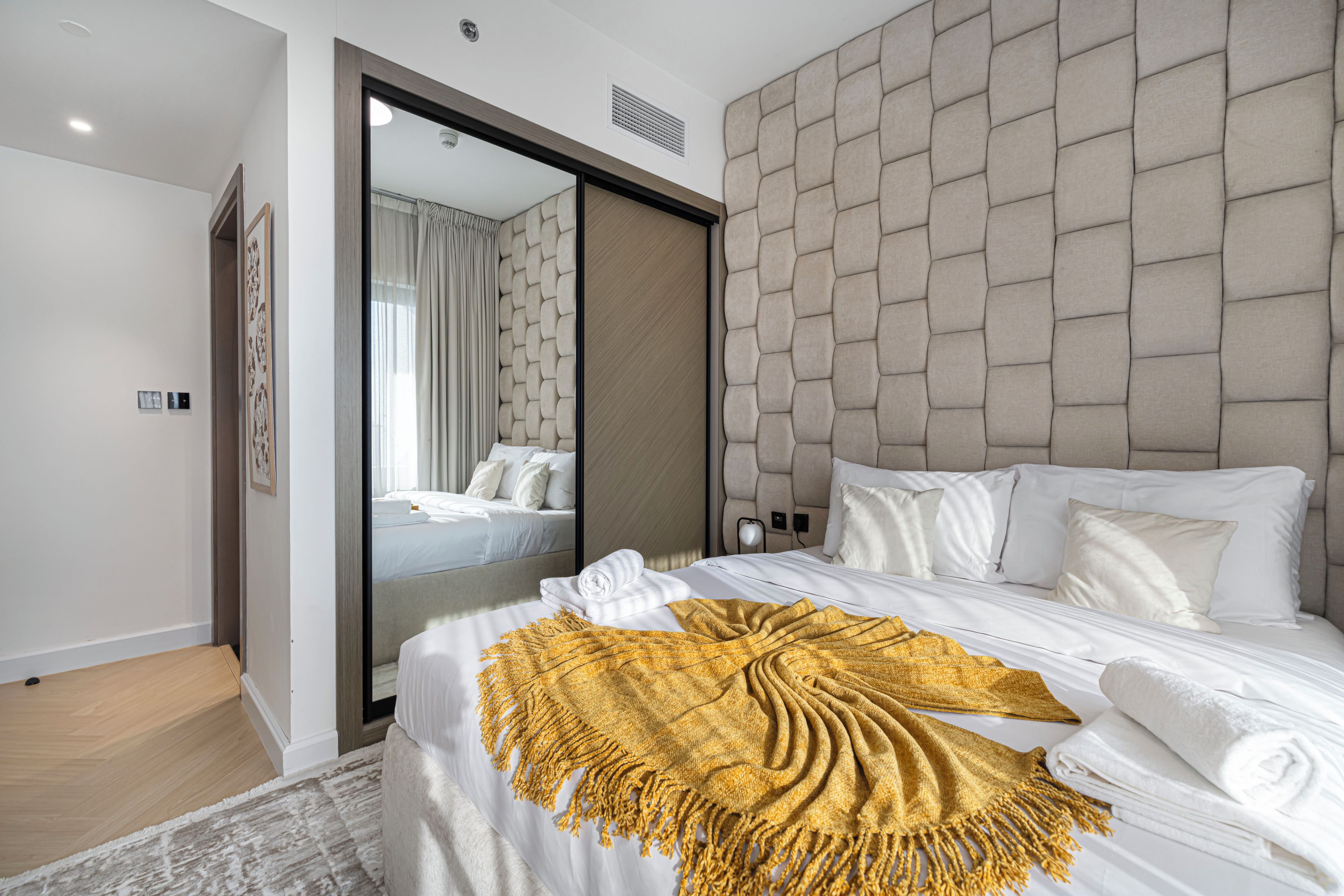 A modern hotel room with a large bed, a mirror, and a headboard with a geometric pattern.