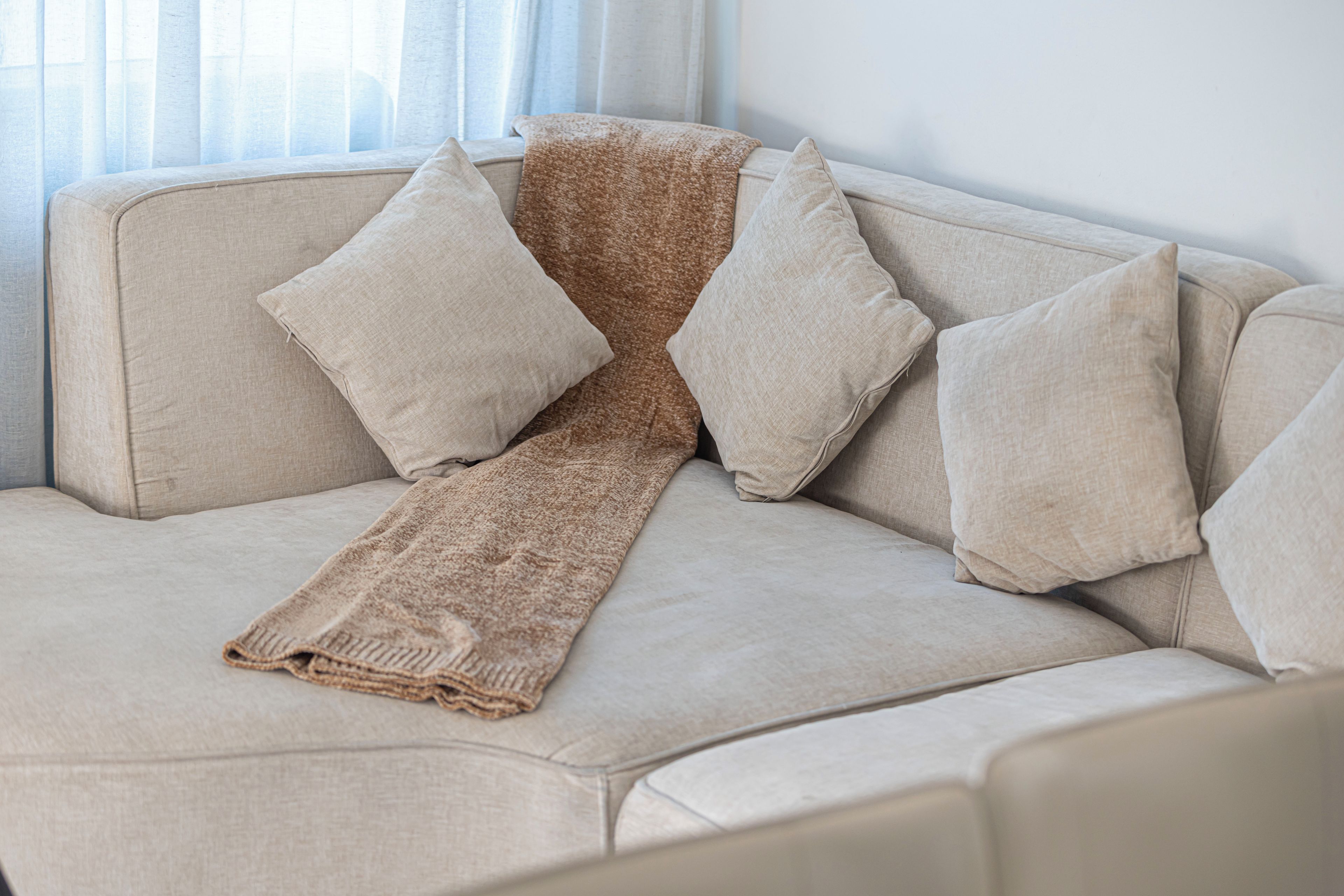A beige sofa with a textured throw blanket and four pillows.