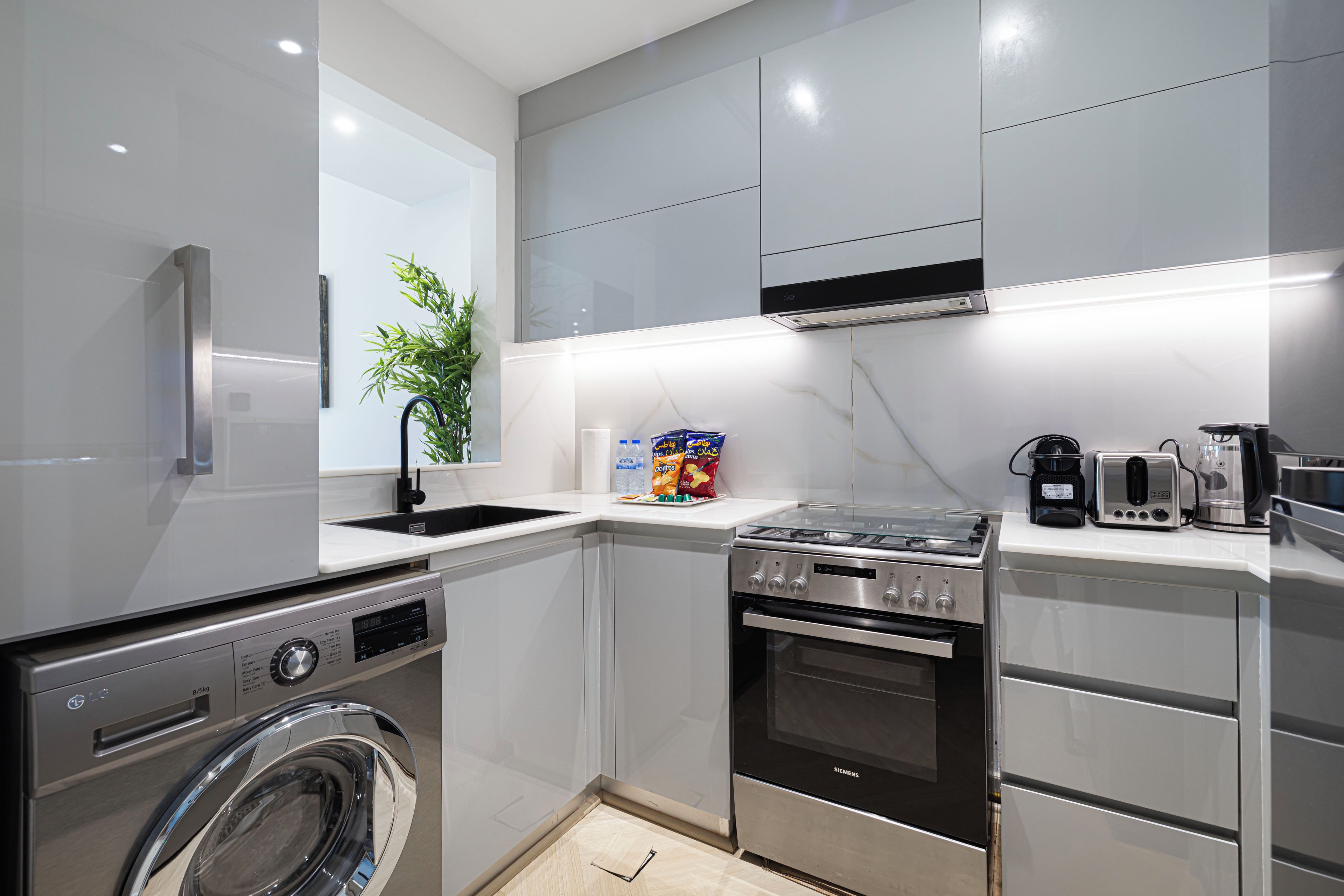 Une cuisine moderne dotée d’appareils électroménagers en acier inoxydable, d’un lave-linge intégré et d’un aménagement compact.
