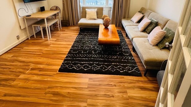 Un soggiorno moderno con pavimento in legno, un divano, un tavolino, una TV e un'ampia finestra con tende.