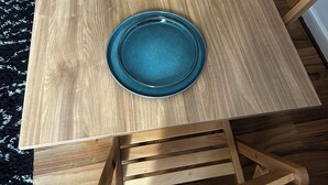 Un tavolo da pranzo in legno con sei piatti blu e posate coordinate, circondato da sedie di legno.